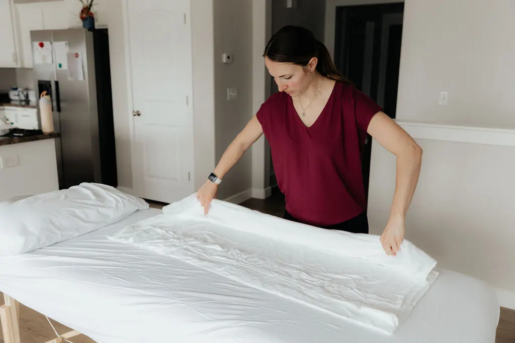 Dr. Danaya Kauwe laying fresh sheets on the treatment table while setting up for an in-home pelvic floor PT session